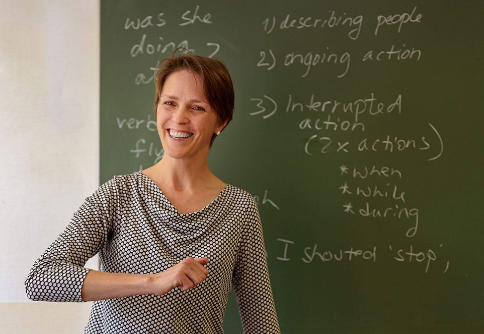 Eine Lehrerin in einem Englischkurs von DIE NEUE SCHULE Sprachschule Berlin vor einer grünen Tafel mit englischen Vokabeln.