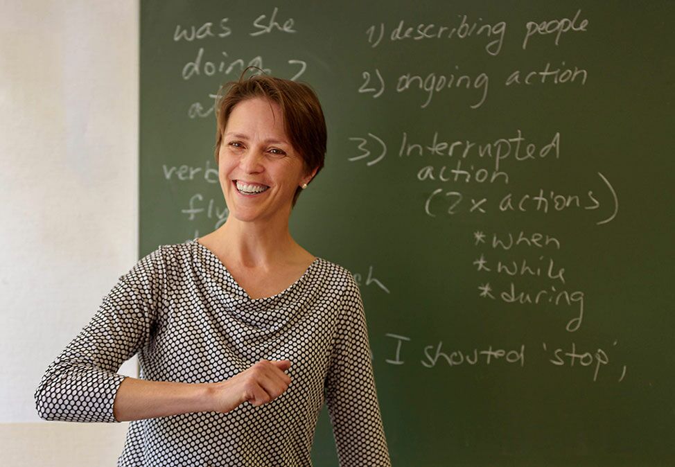 A teacher in an English course at DIE NEUE SCHULE Sprachschule Berlin in front of a green board with English vocabulary